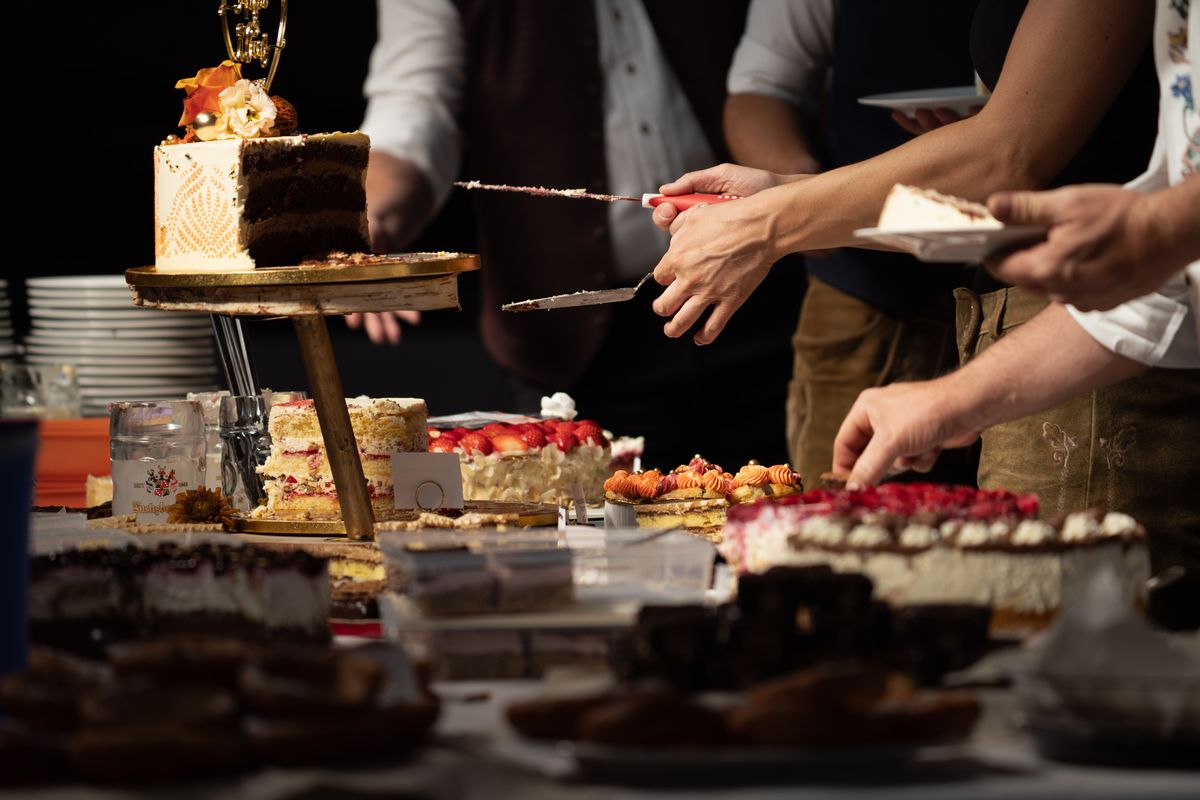 Guests helping themselves to slices from a table of birthday cakes and desserts