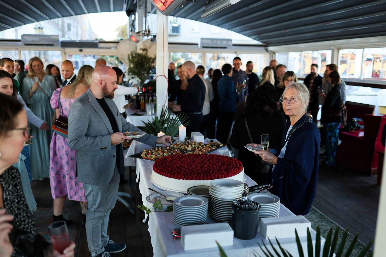 Guests of all ages helping themselves from a birthday party buffet table with a large berry cake in the middle