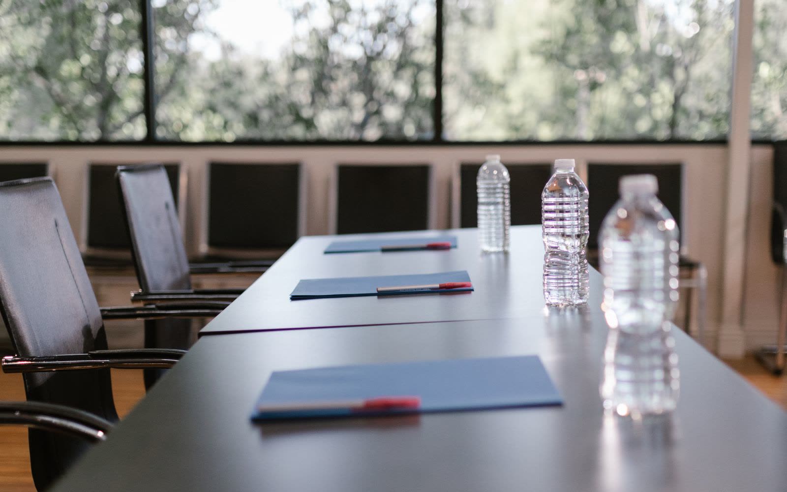 A meeting room laid out with pads, pens and bottled water along a boardroom table