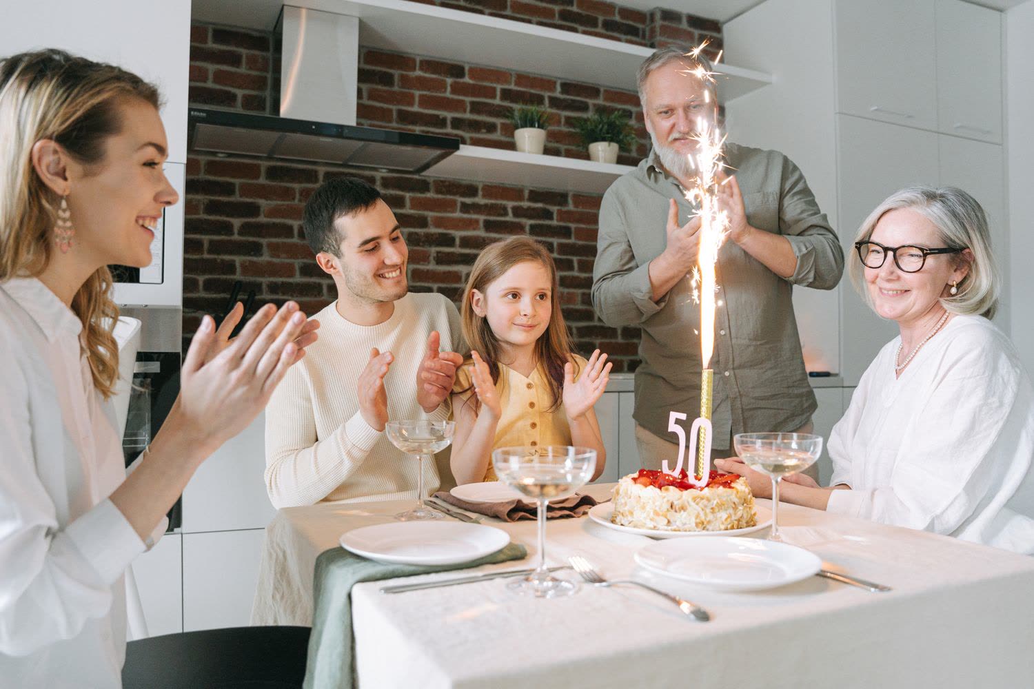 Three generations of a family clapping around a 50th birthday cake with a lit sparkler candle