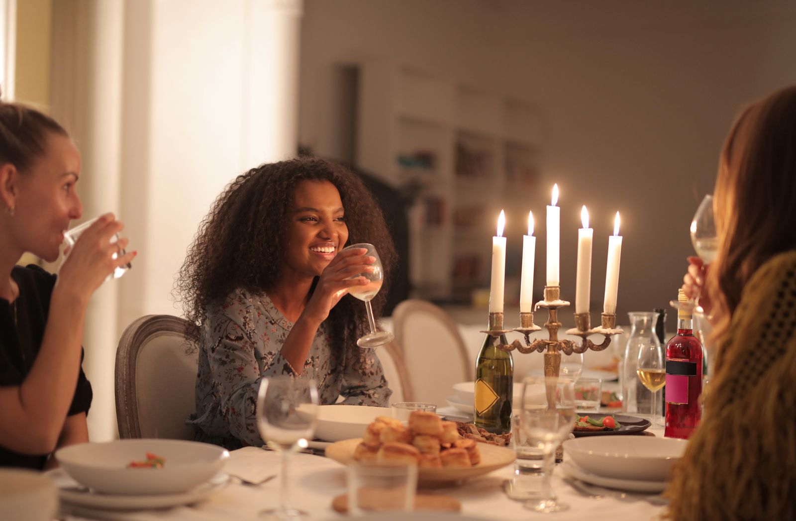 A small candlelit dinner party, four friends around one table with wine glasses and a candelabra