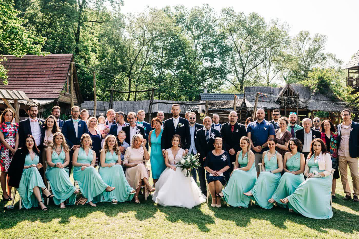 A large wedding group photo of the couple with their families and guests posed together outdoors
