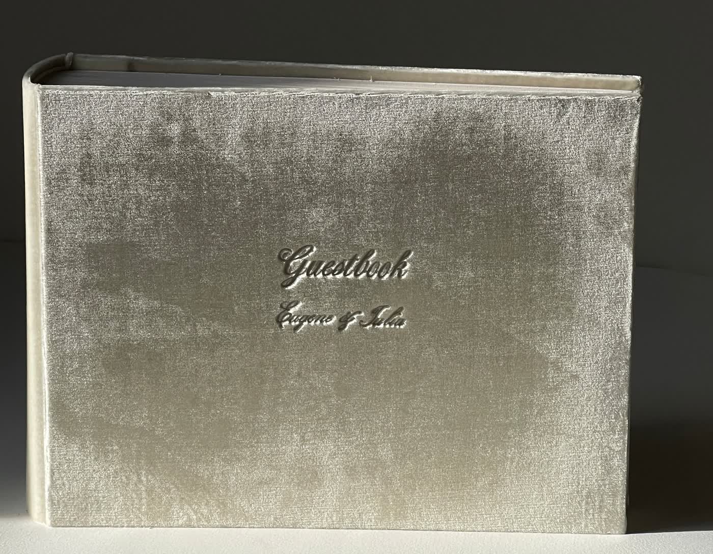 A cream velvet wedding guest book cover embossed with the word Guestbook and the couple’s first names