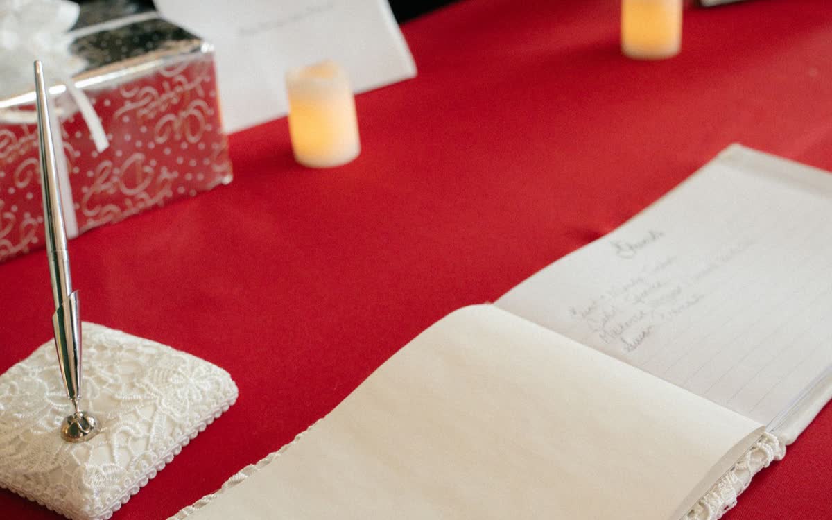 An open wedding guest book on a red tablecloth with a pen stand and candles nearby