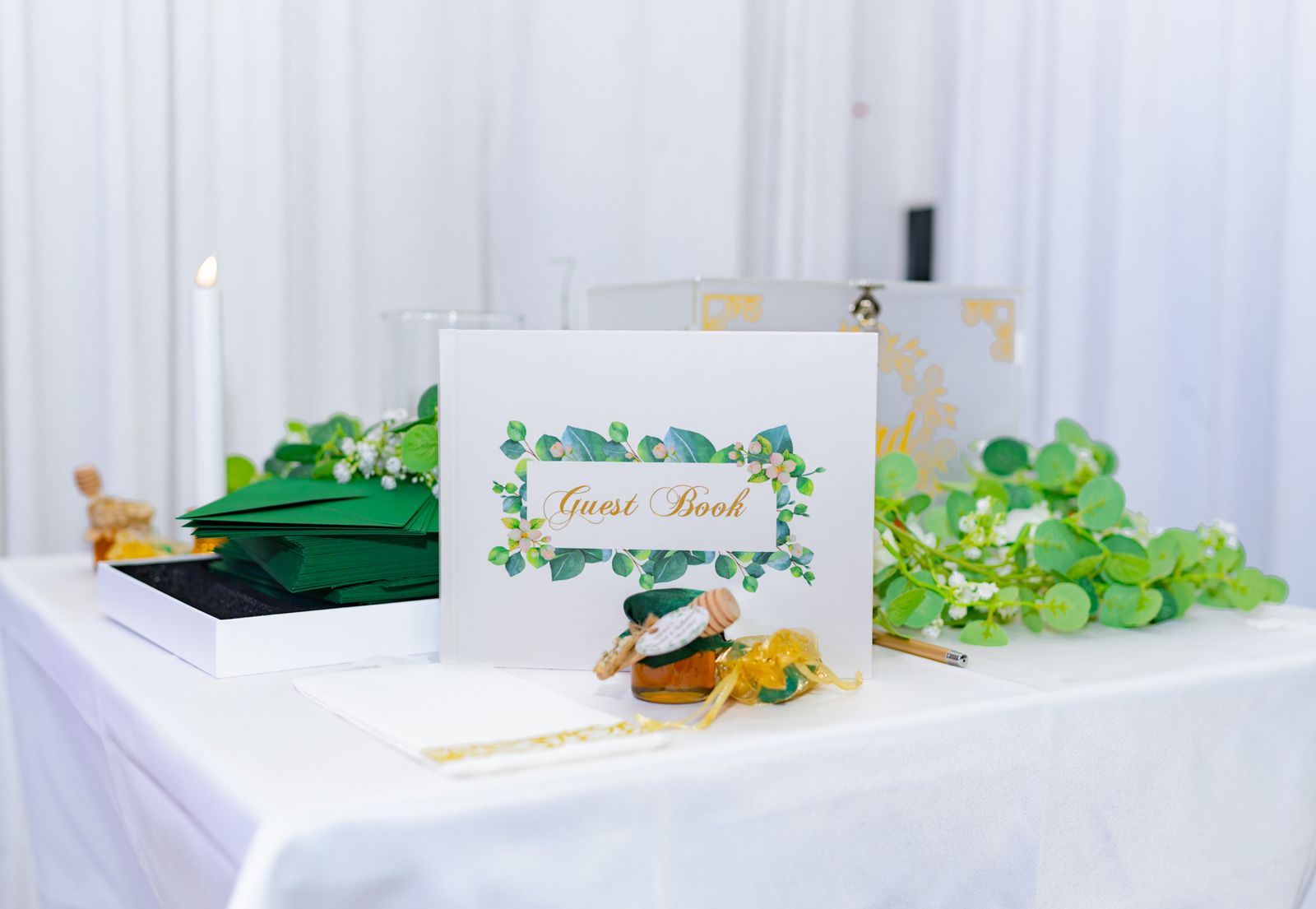 A wedding guest book with green floral decoration open on a white table, ready for guests to sign