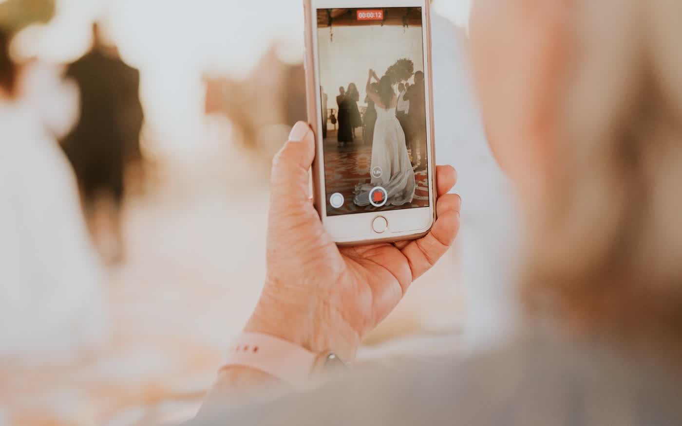 Over the shoulder view of a wedding guest filming the couple on a phone, with the video recording timer showing twelve seconds