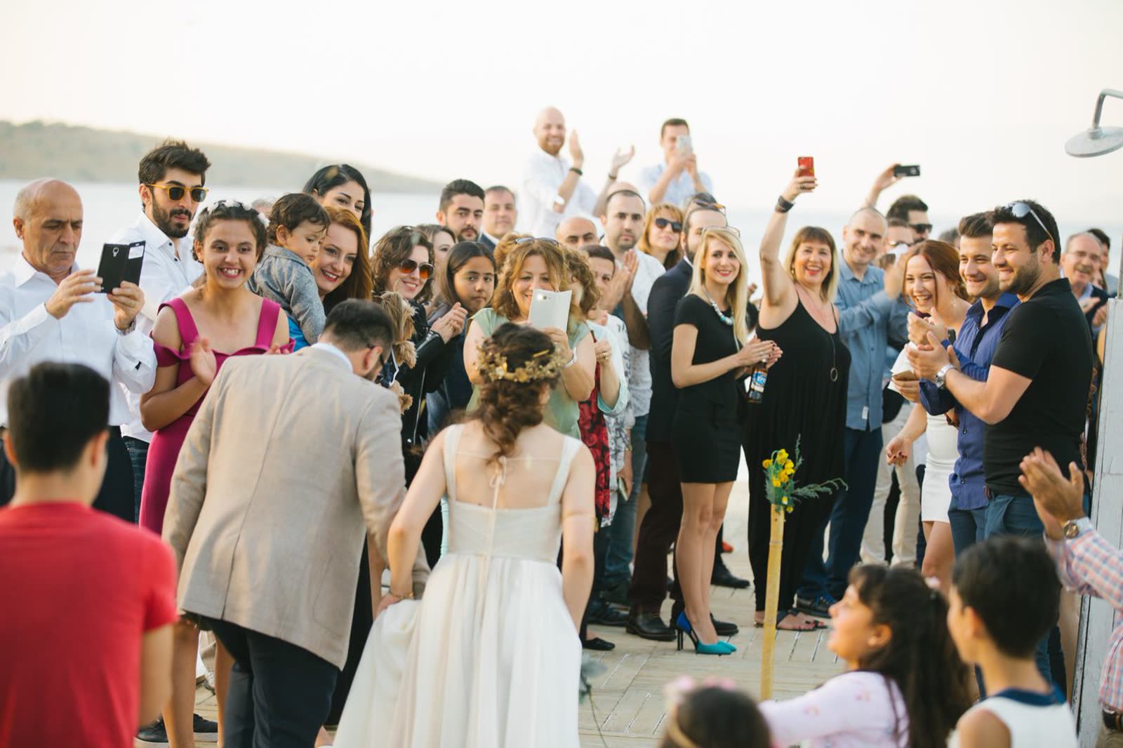 Wedding guests crowded along an aisle holding up phones and cameras to photograph the couple