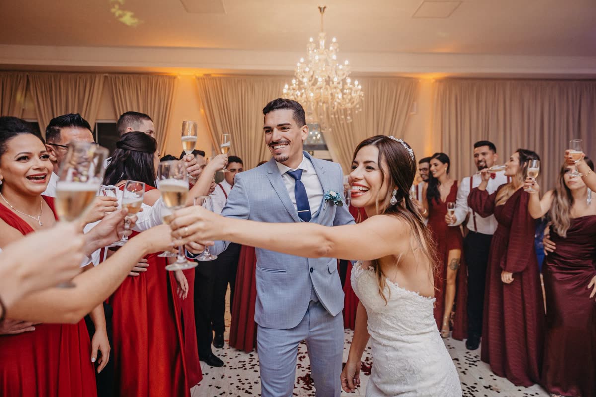 Wedding guests crowding round a bride and groom, raising champagne glasses in a chandeliered reception room