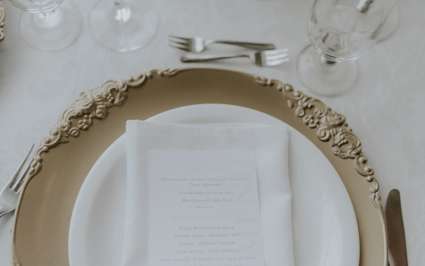 An overhead wedding place setting with a printed menu card folded into a white napkin on a gold charger plate