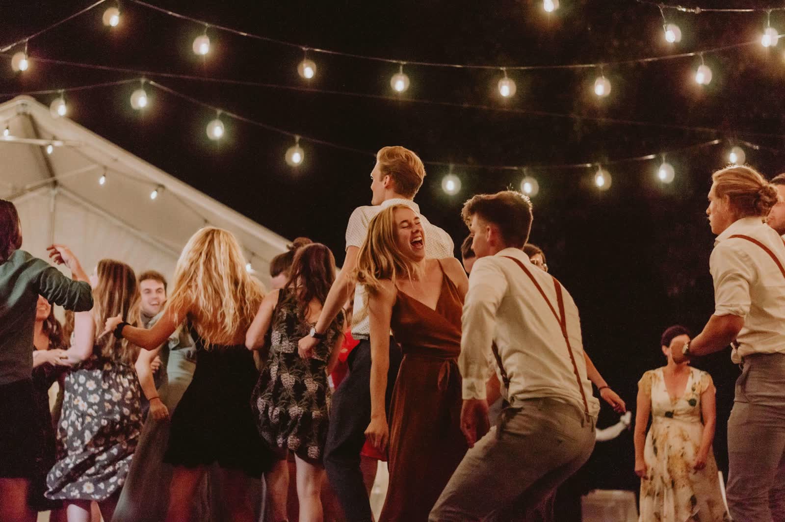 Wedding guests dancing under strings of warm lights at an evening tented reception
