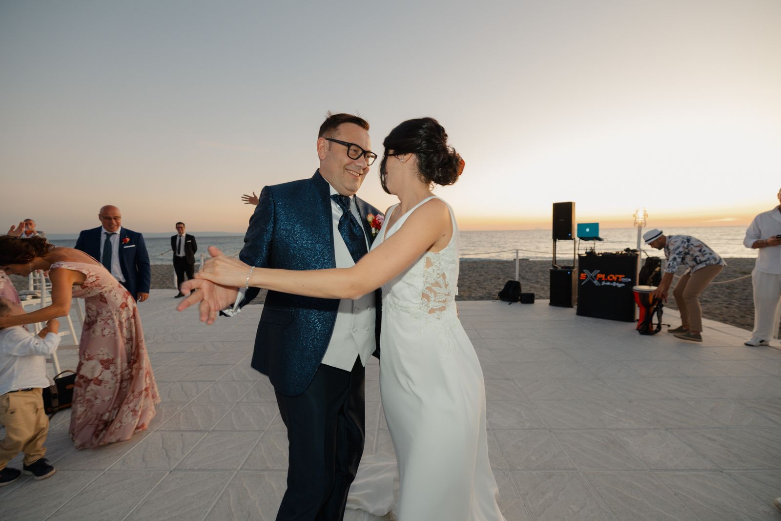 A couple dancing joyfully at their beachfront wedding reception during sunset