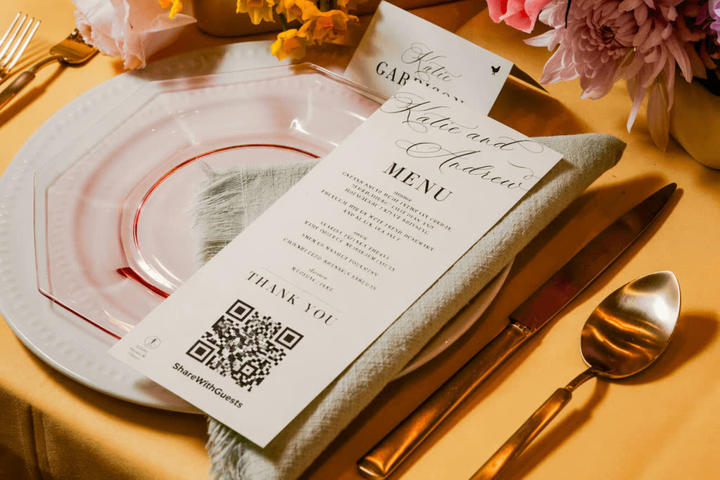 A wedding reception place setting with a printed menu card, gold cutlery and bright florals