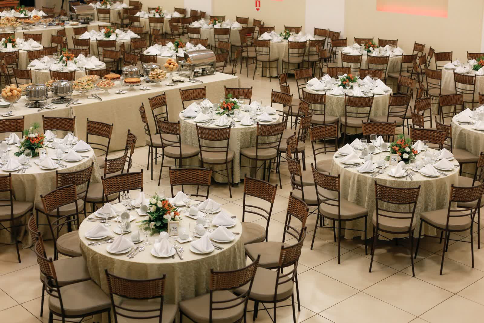 A wedding reception hall fully set with round dining tables, place settings and floral centrepieces, ready for guests to be brought back in after the room flip