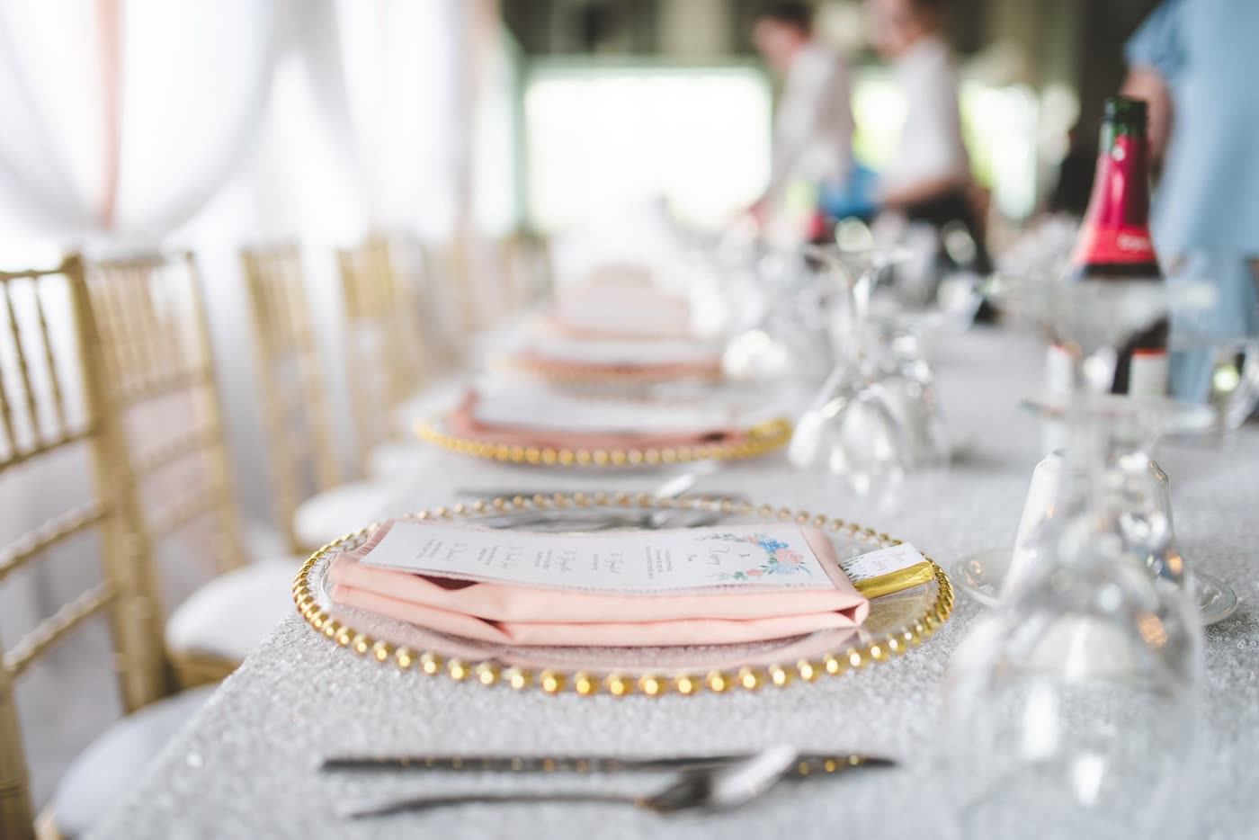 A wedding reception table run with printed menu cards laid on gold charger plates and blush napkins
