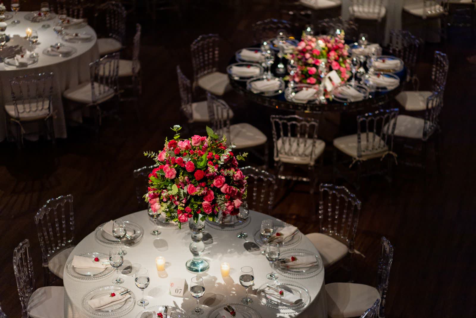An elegant wedding reception room set with round tables, rose centerpieces and a numbered table card in the foreground