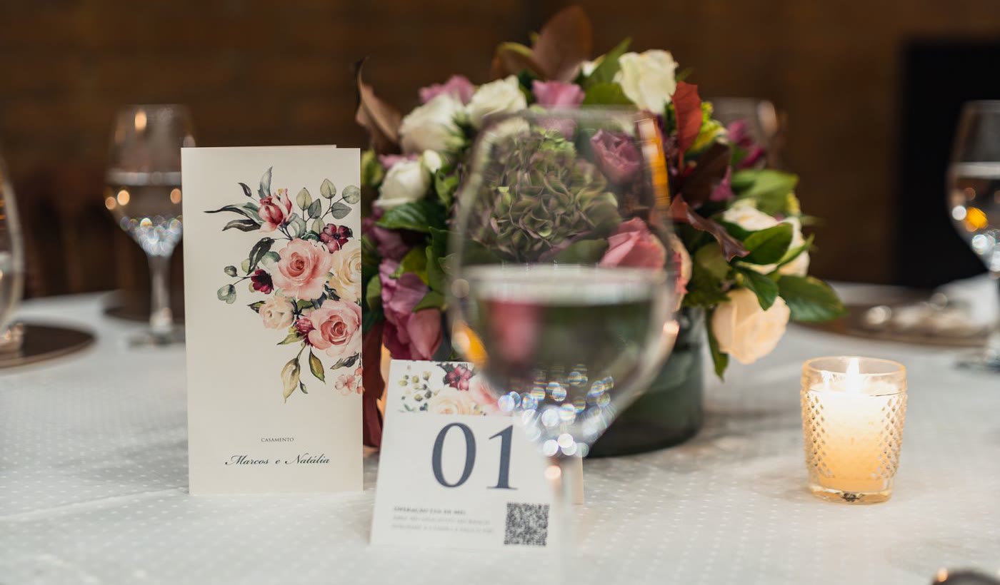 A wedding reception table setting with a QR code printed on the table number card, next to a floral centerpiece and candle